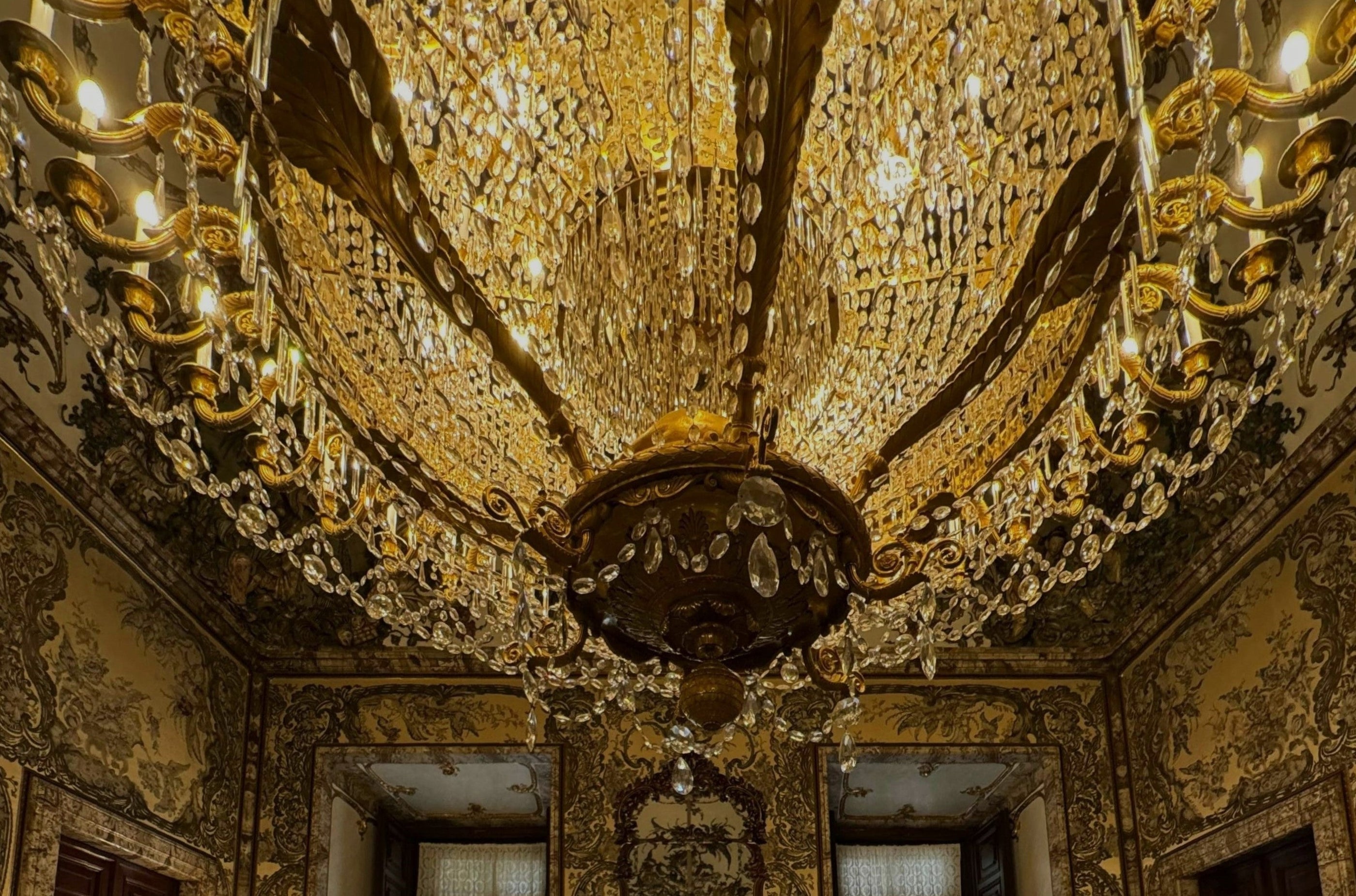 Luxury room with large chandelier with many crystals on the ceiling with cream marble floors and vintage designed wallpaper.