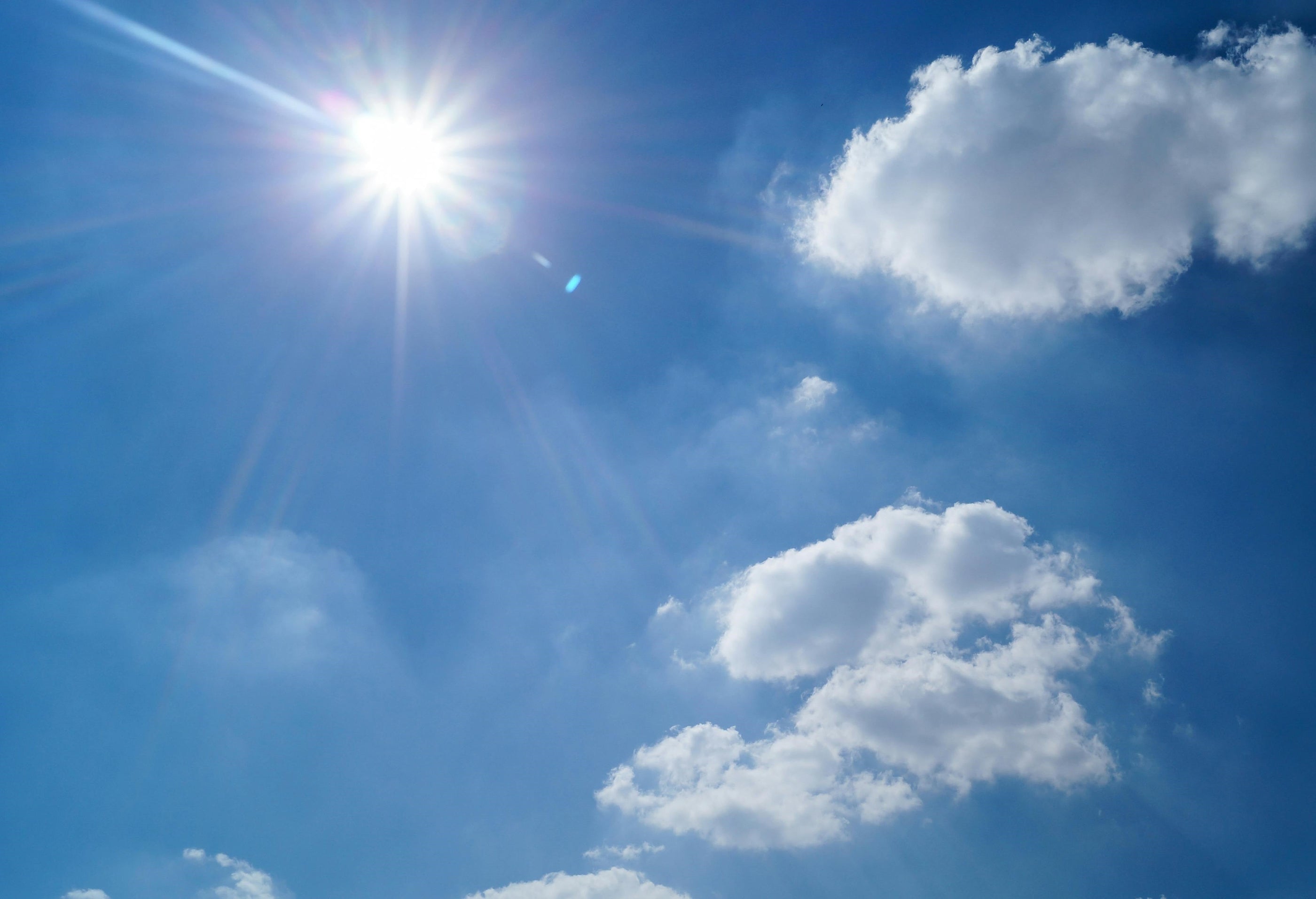 Bright sunshine in the blue sky next to fluffy white clouds.