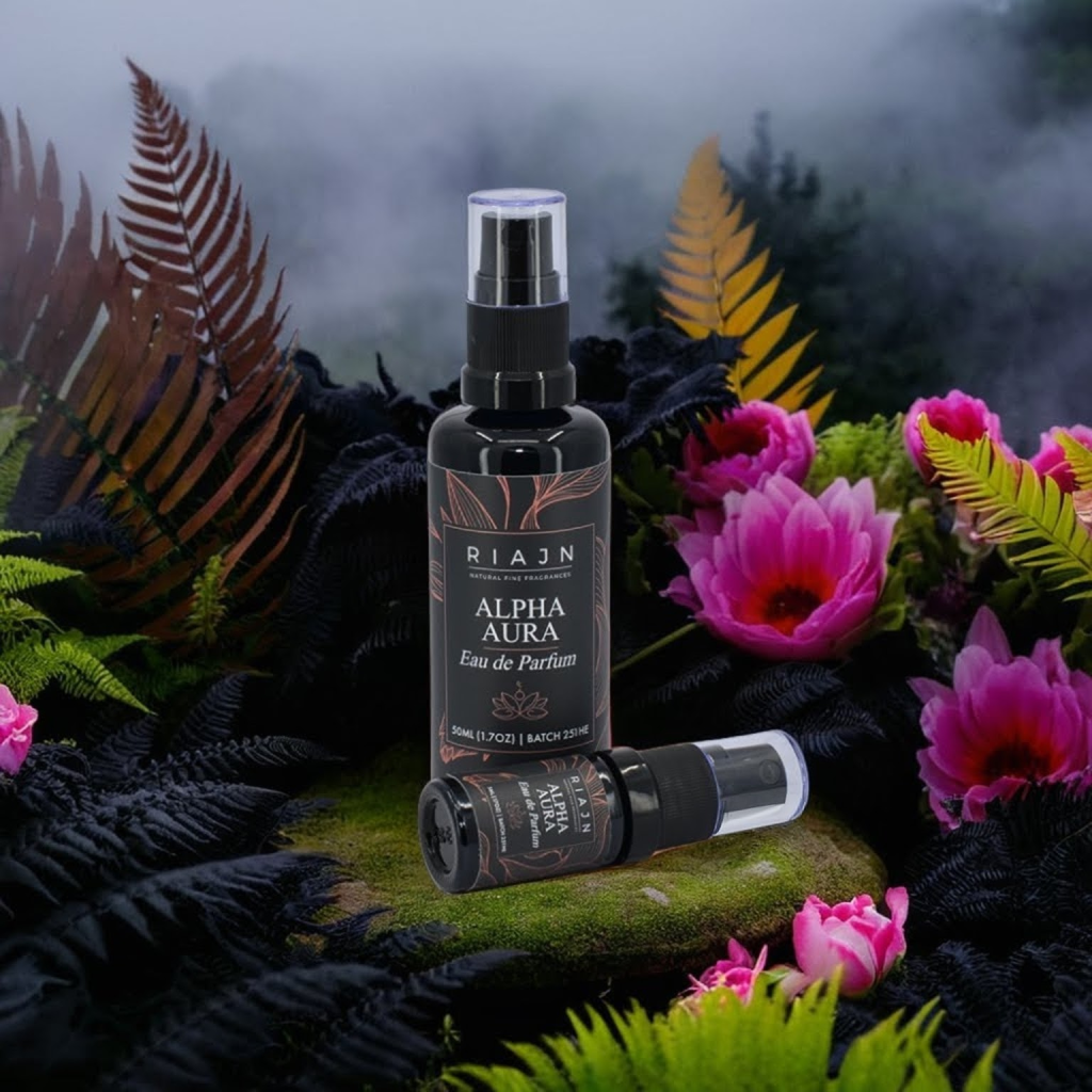 RIAJN Alpha Aura EDP bottles sitting on a rock with moss surrounded by black ferns and bright pink blooming flowers with fog in the background