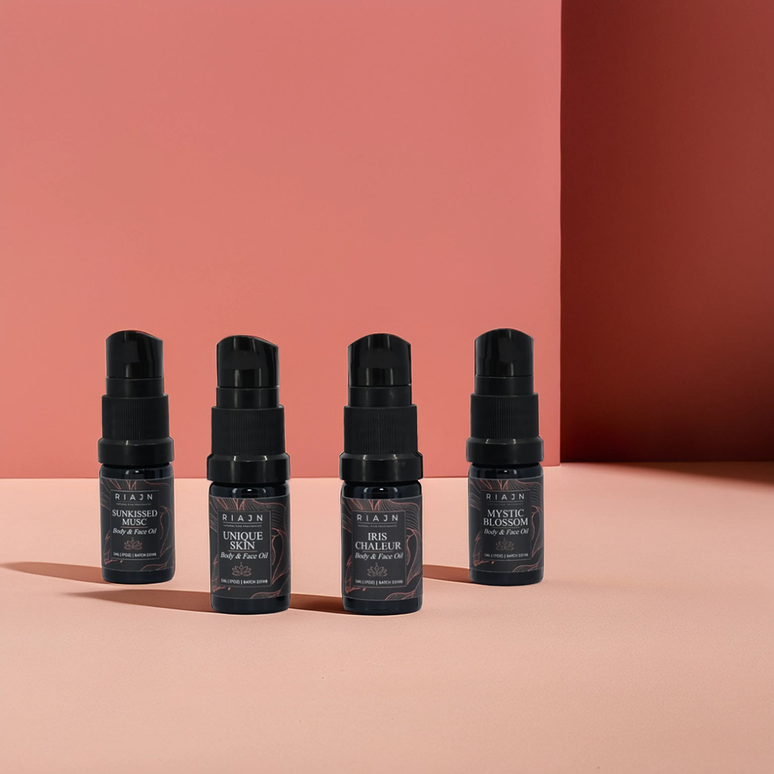RIAJN Body Oil Sample Set bottles standing on a light pink floor with a dark pink wall with shadows. Best skin moisturizer for face and body oil.