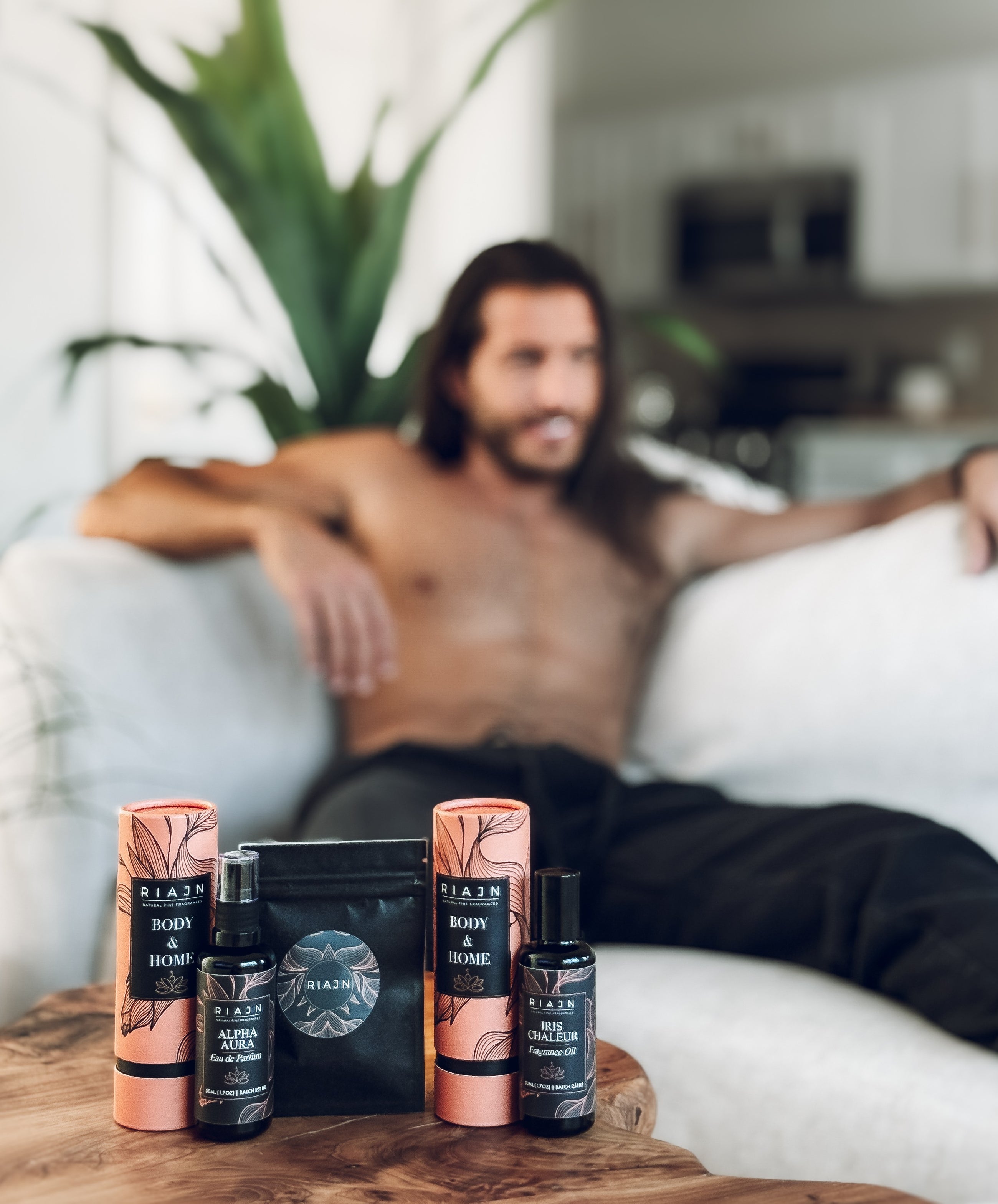 Man sitting on a couch with Riajin body care products on a table in front of him.
