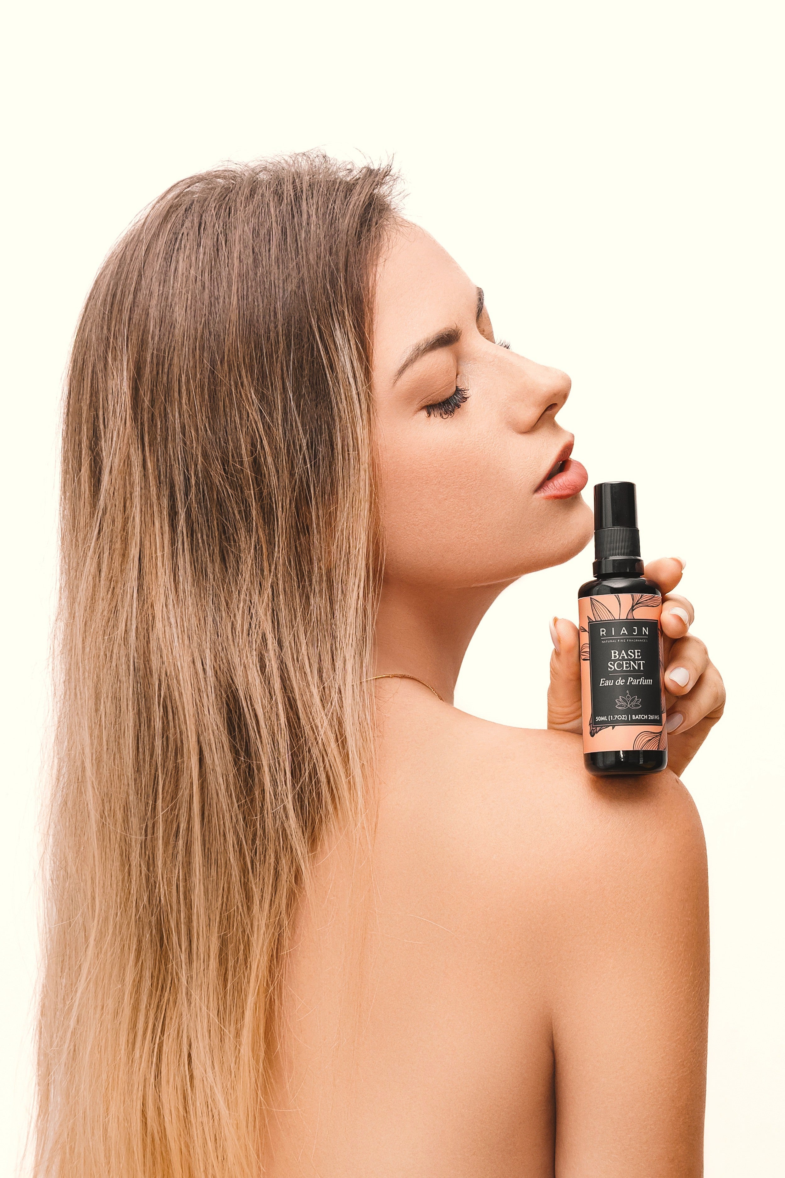 Woman holding a RIAJN base scent bottle of hair product over her shoulder against a white background