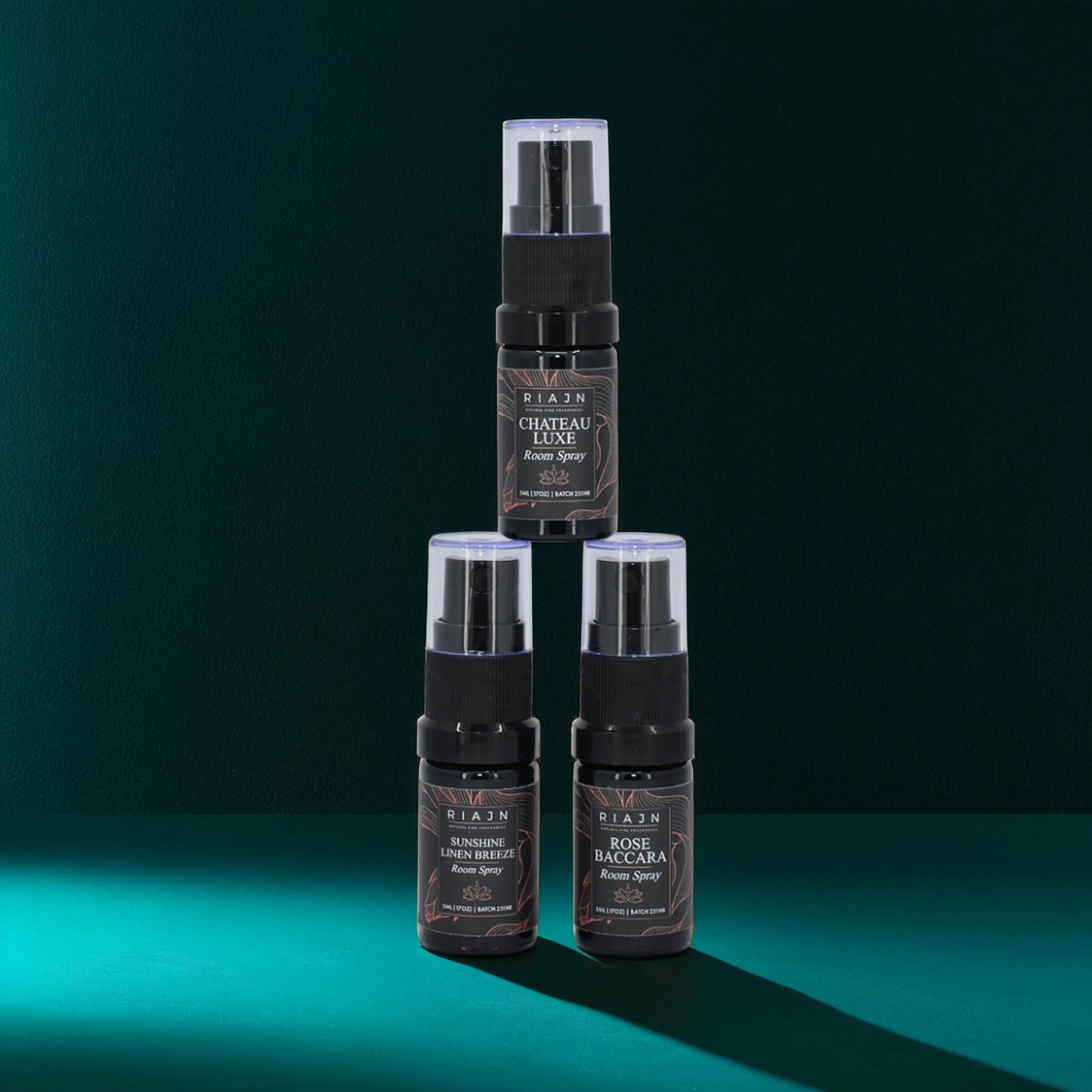 RIAJN Room Spray Sample Set bottles stacked in a turquoise room with soft shadows. Long lasting room spray.