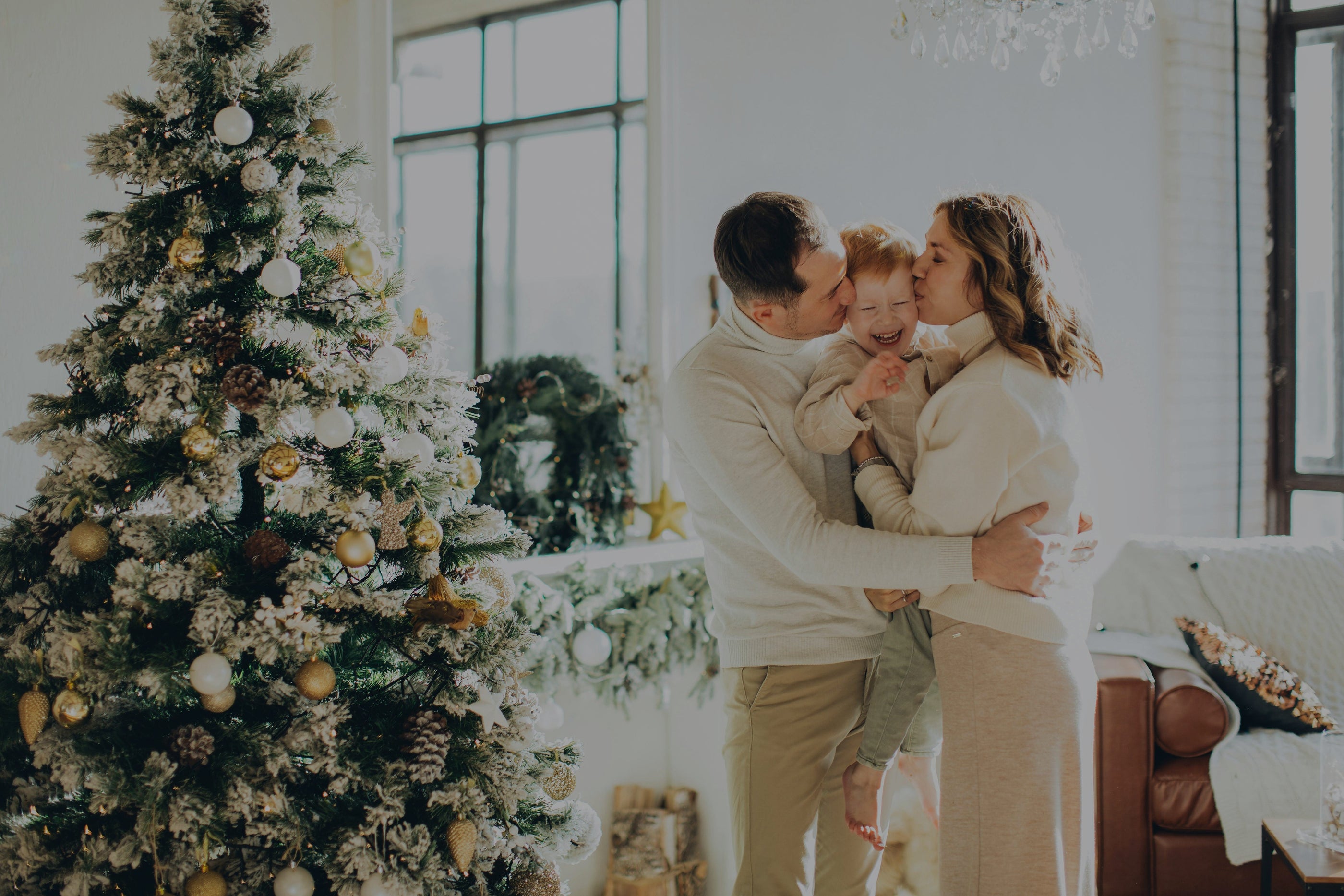 Mother and father kissing son they are holding in between them near a decorated Christmas tree. Top long lasting air fresheners, best room sprays, and popular reed diffusers.