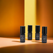 RIAJN Fragrance Oil Sample Set bottles standing in a v-formation with orange floor and yellow and orange background with soft shadows. Top perfume oils for woman and men.