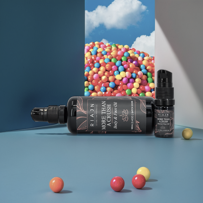 Two bottles of RIAIN More Than a Crush body and face serum with colorful candy balls on a blue background