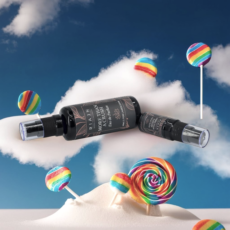 Two bottles of More Than a Crush eau de parfum on a cloud with rainbow lollipops against a blue sky.