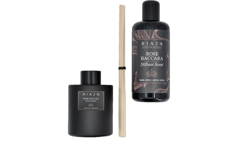 Two black bottles of RIAJN's rose baccara home fragrance scent next to a black diffuser bottle and wooden diffuser sticks on a white background