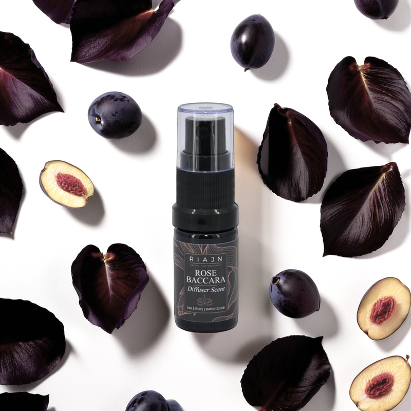 RIAJN Rose Baccara diffuser spray surrounded by dark purple leaves and figs on a white background