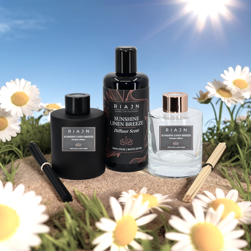 Three RIAN diffuser scents and glass diffuser bottles on sand with daisies and a blue sky